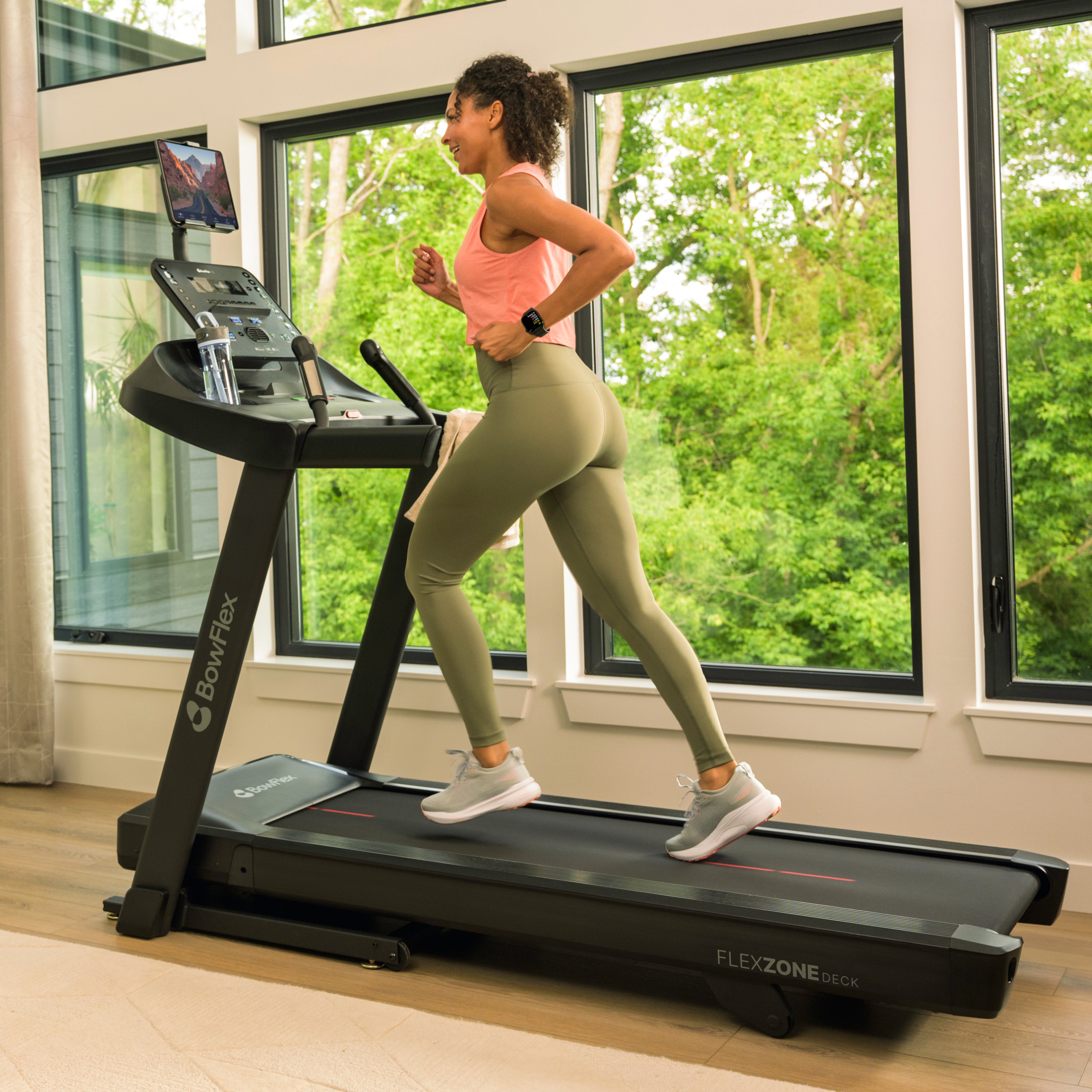 Woman running on a BowFlex T6 treadmill in a bright home gym setting.
